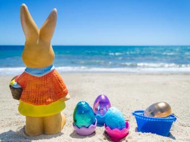 Coniglietto pasquale e uova colorate sulla spiaggia soleggiata.